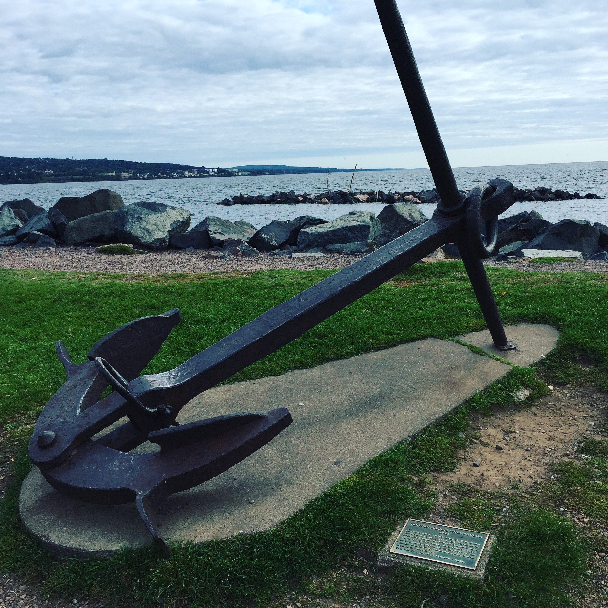 a large anchor on a concrete platform on grass by a body of water